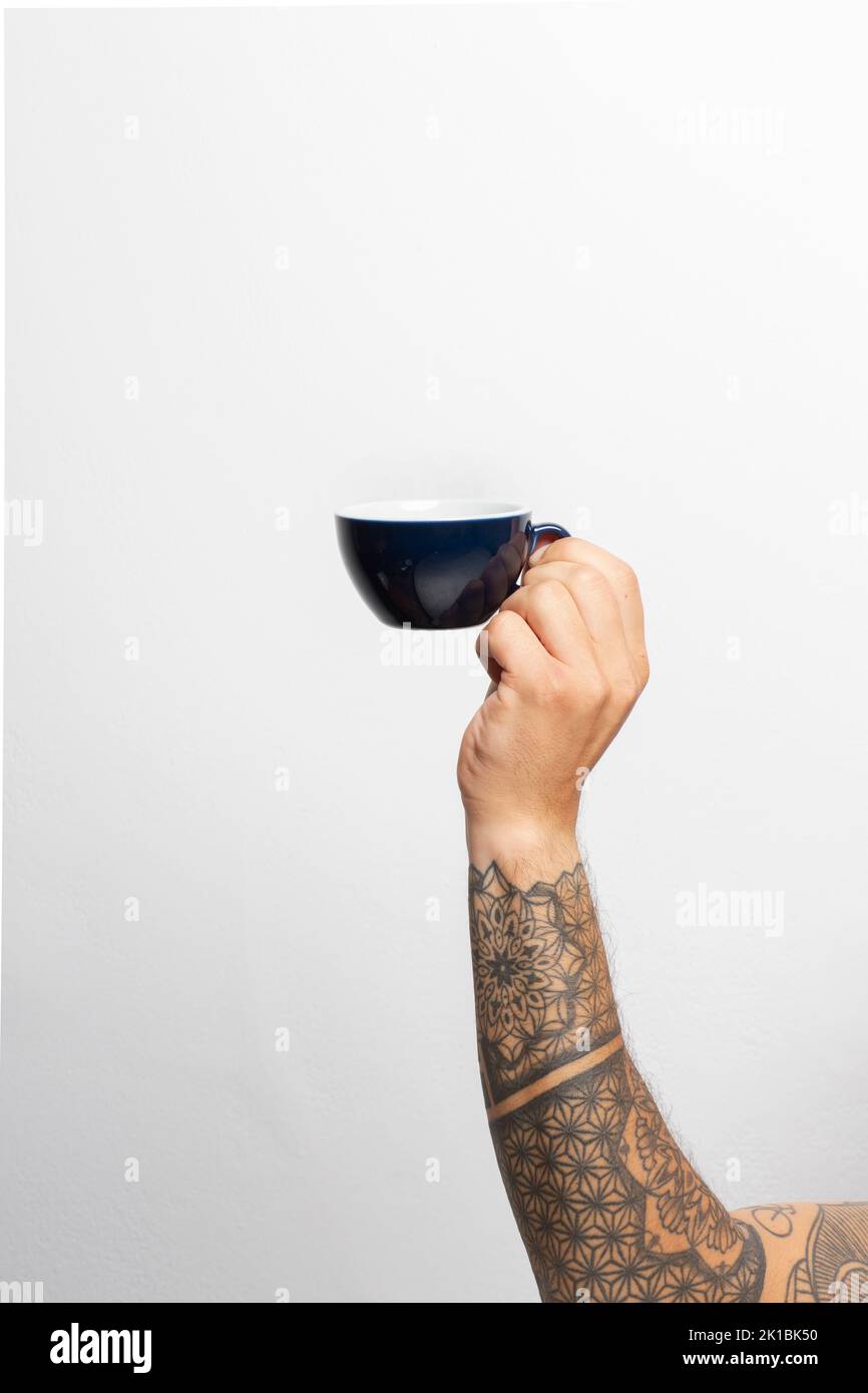 Nahaufnahme`s Arm und Hand eines tätowierten Mannes mit einer Kaffeetasse vor weißem Hintergrund Stockfoto